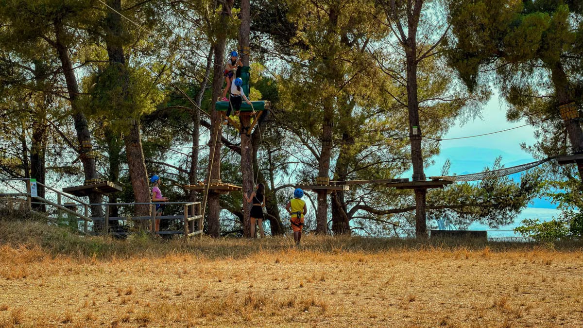 Outdoor adventure park with people navigating tree obstacles in Liguria, Italy.